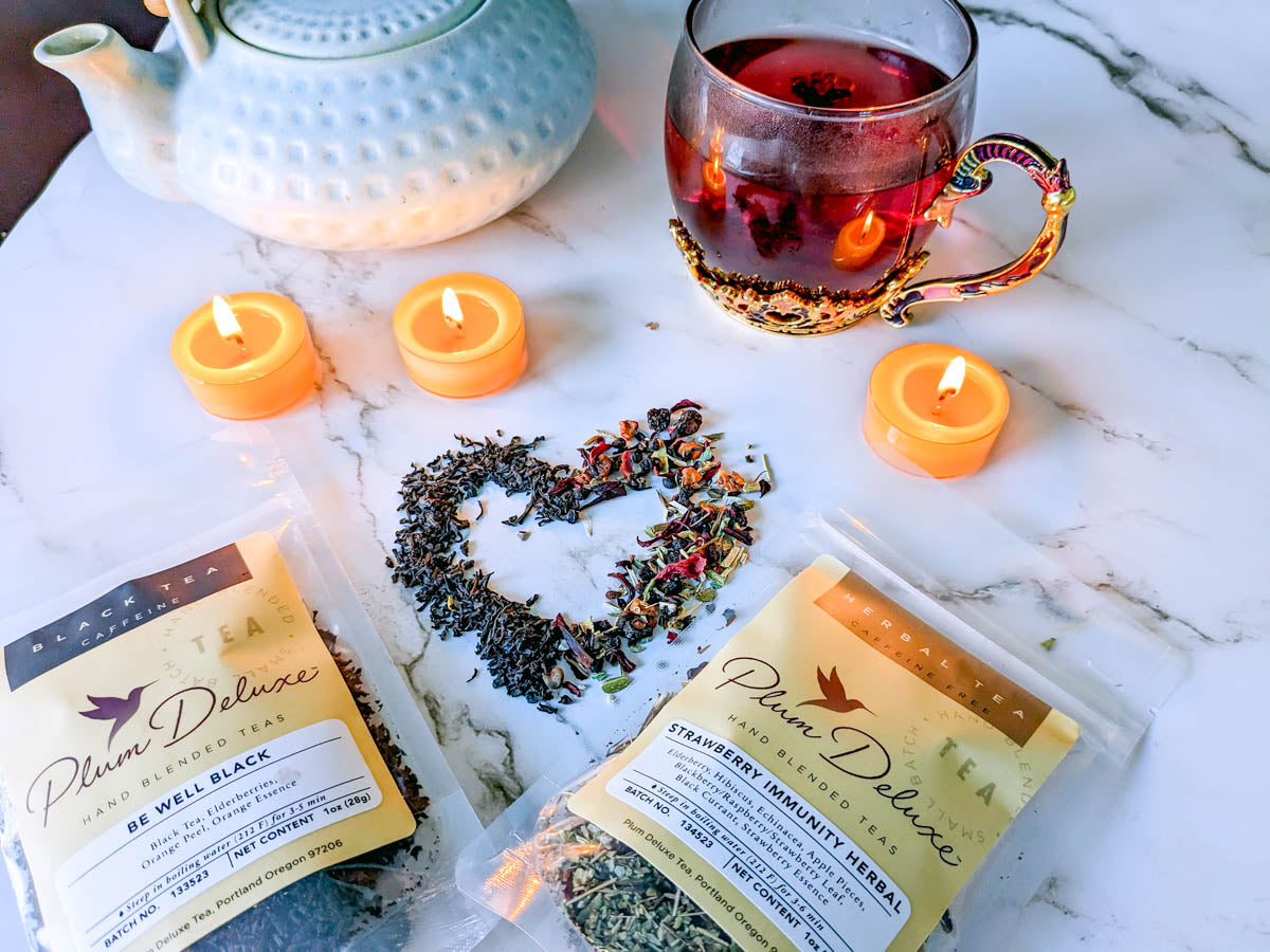 A spread of plum deluxe loose-leaf immunity teas shaped into a heart, accompanied by candles and a cup of tea.