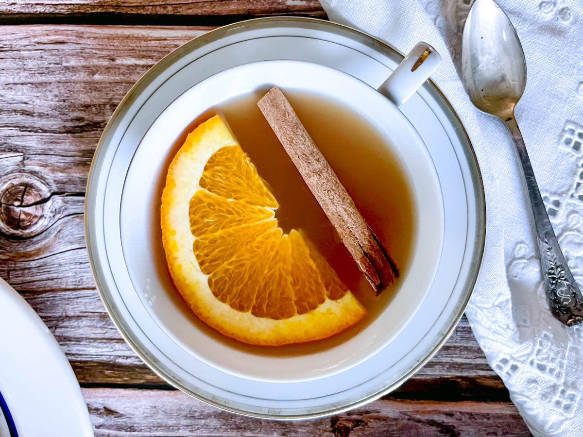 A cup of mulled cider topped with a fresh orange slice and a cinnamon stick.