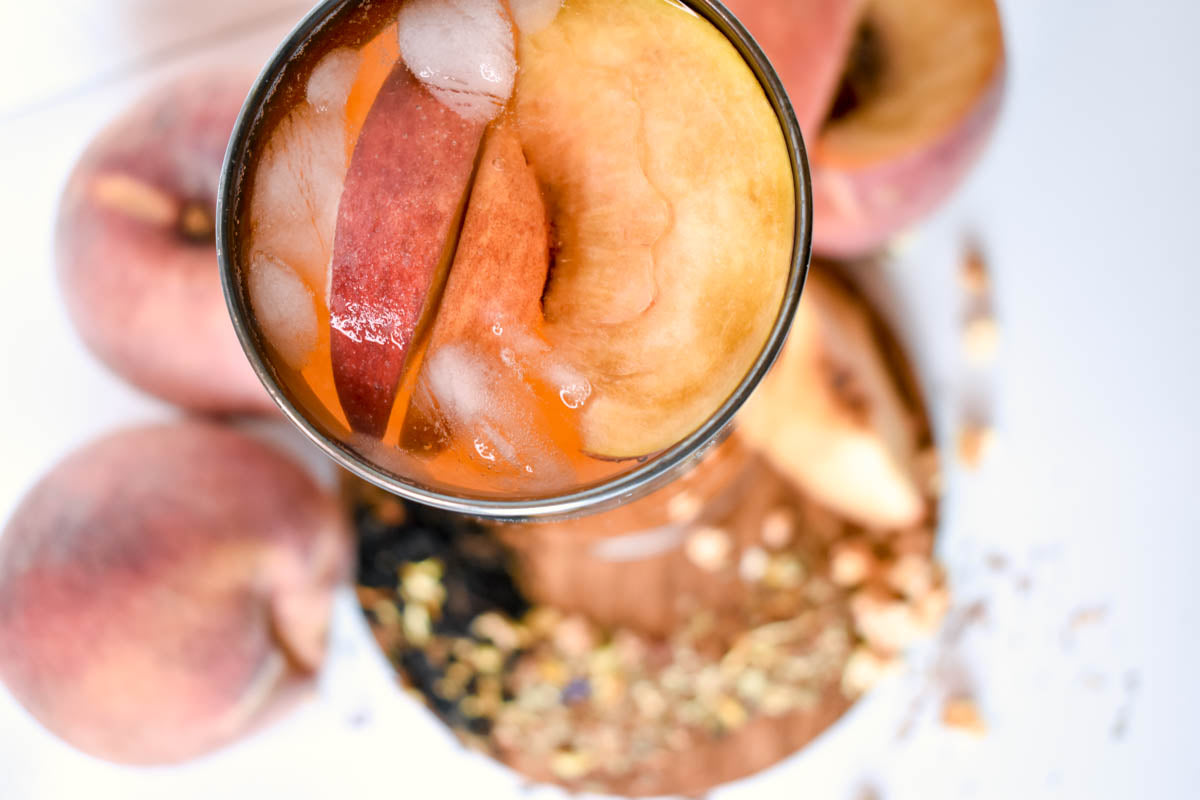 This close-up top-down view of the peach tea glass highlights the ice and fresh peach slices used as a garnish.