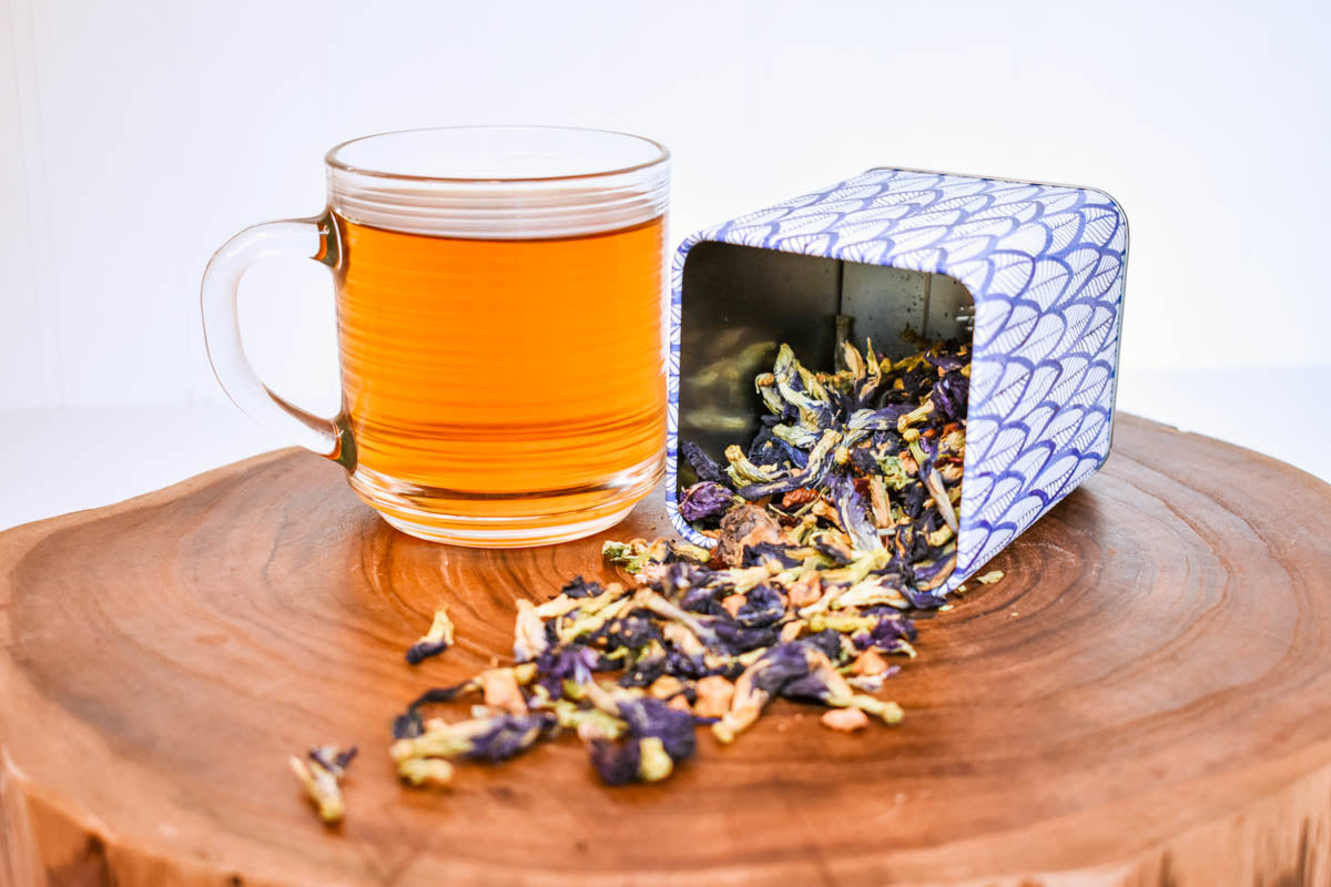 A glass of tea and Magical Butterfly loose-leaf herbal tea in a tea tin.