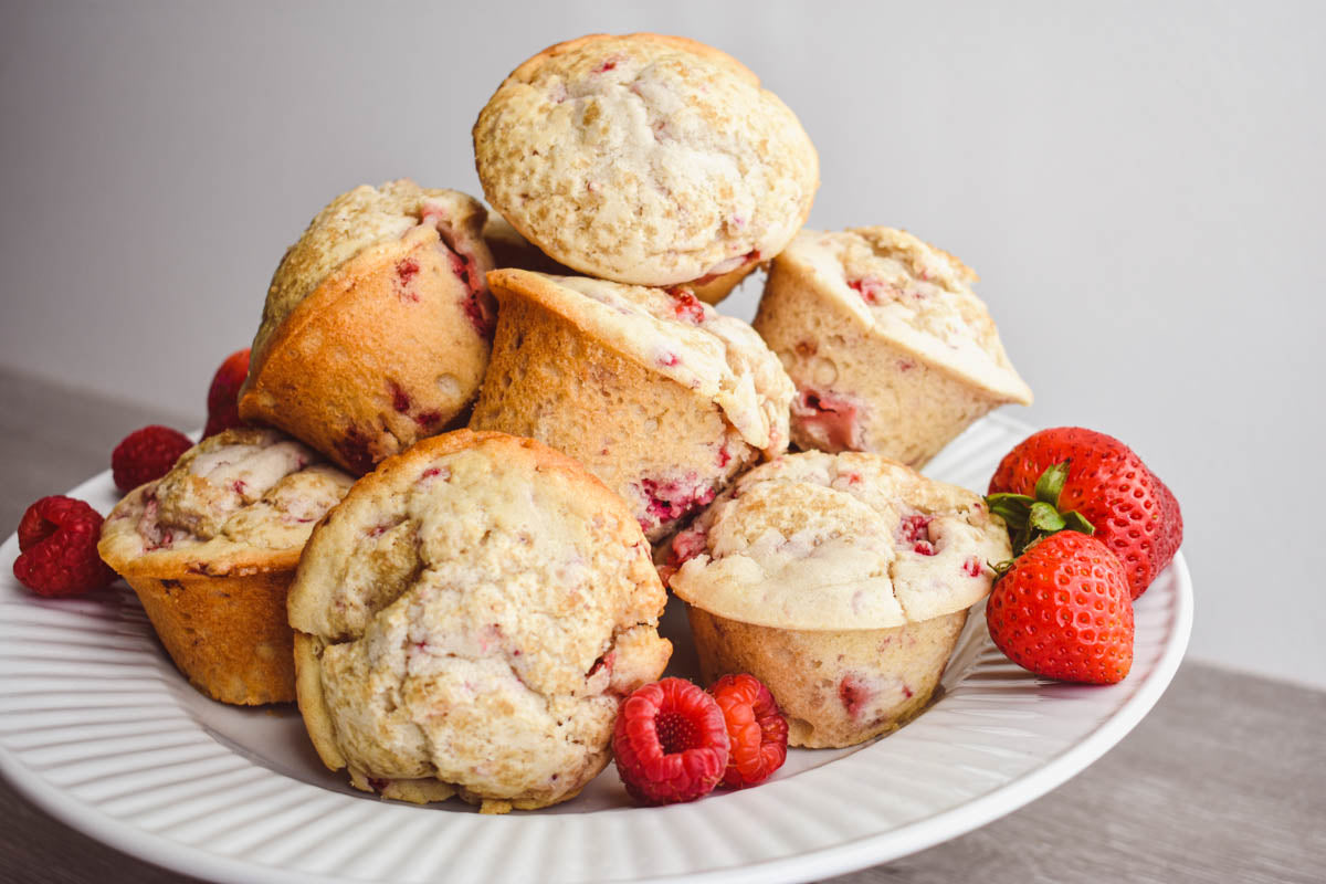 A plate of fresh berry scones since on a wooden surface, with strawberries and raspberries sitting on the side of the plate.