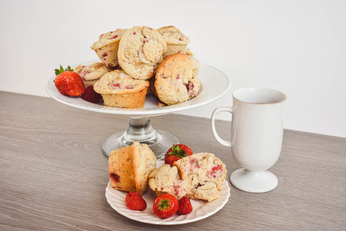 A plate and platter of berry scones and fresh strawberries and raspberries sits on a wooden table, next to a up of tea.