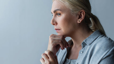 Blonde women in light blue button up shirt thinking in front of a grey/blue wall.