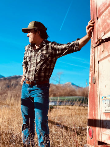 Mack standing in the scenic Montana wilderness, proudly wearing a Mack Belt that symbolizes resilience and craftsmanship.