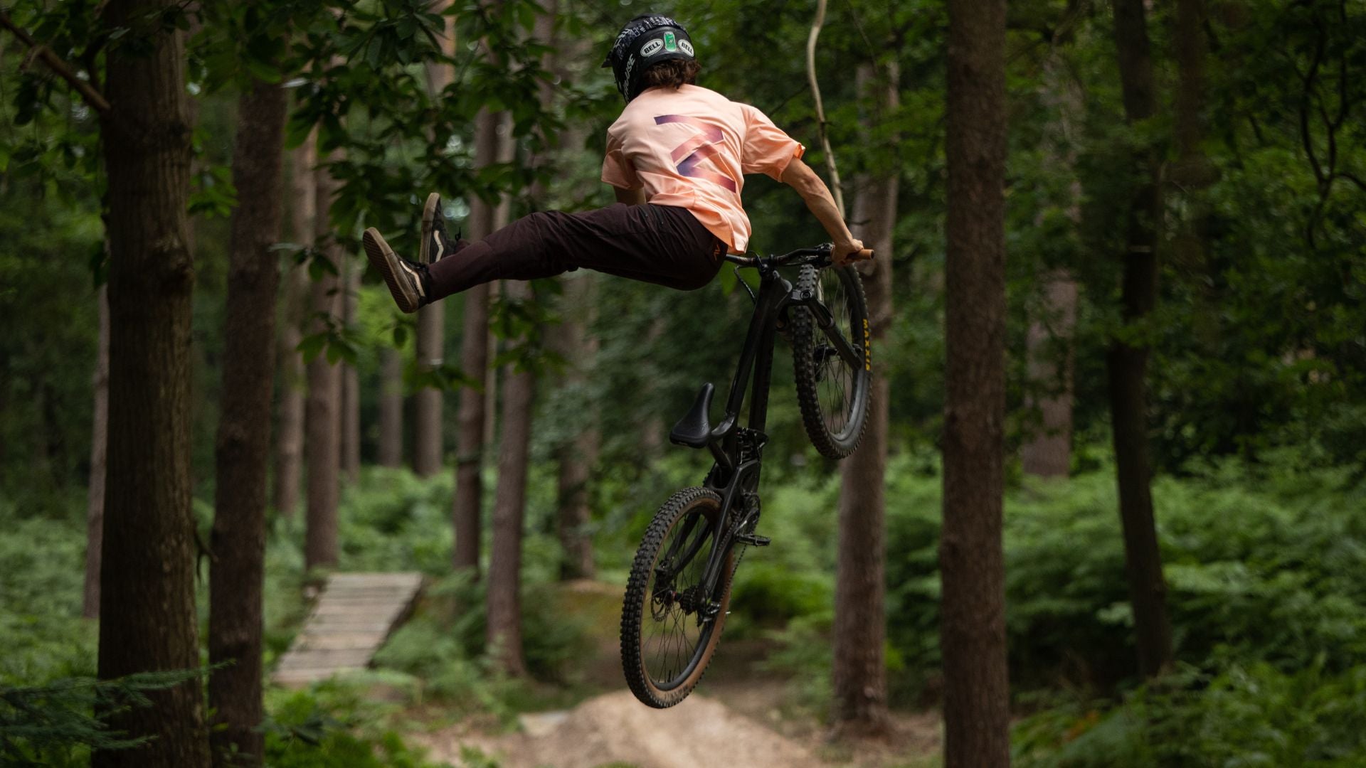 Mountain biker in mid-jump on a downhill course, wearing durable MTB pants, showcasing their strength and ability to withstand extreme riding conditions.