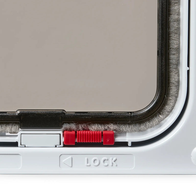 Close-up view of the right hand corner of a white cat door frame with a red manual lock, clear flap and grey draft proof brushing above a 'Lock' label, on a white background 