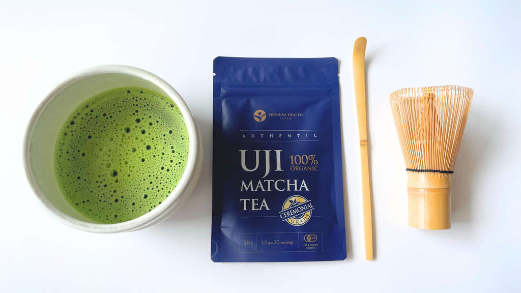 Matcha bowl filled with frothy matcha, packet of Uji matcha tea, bamboo matcha scoop and whisk