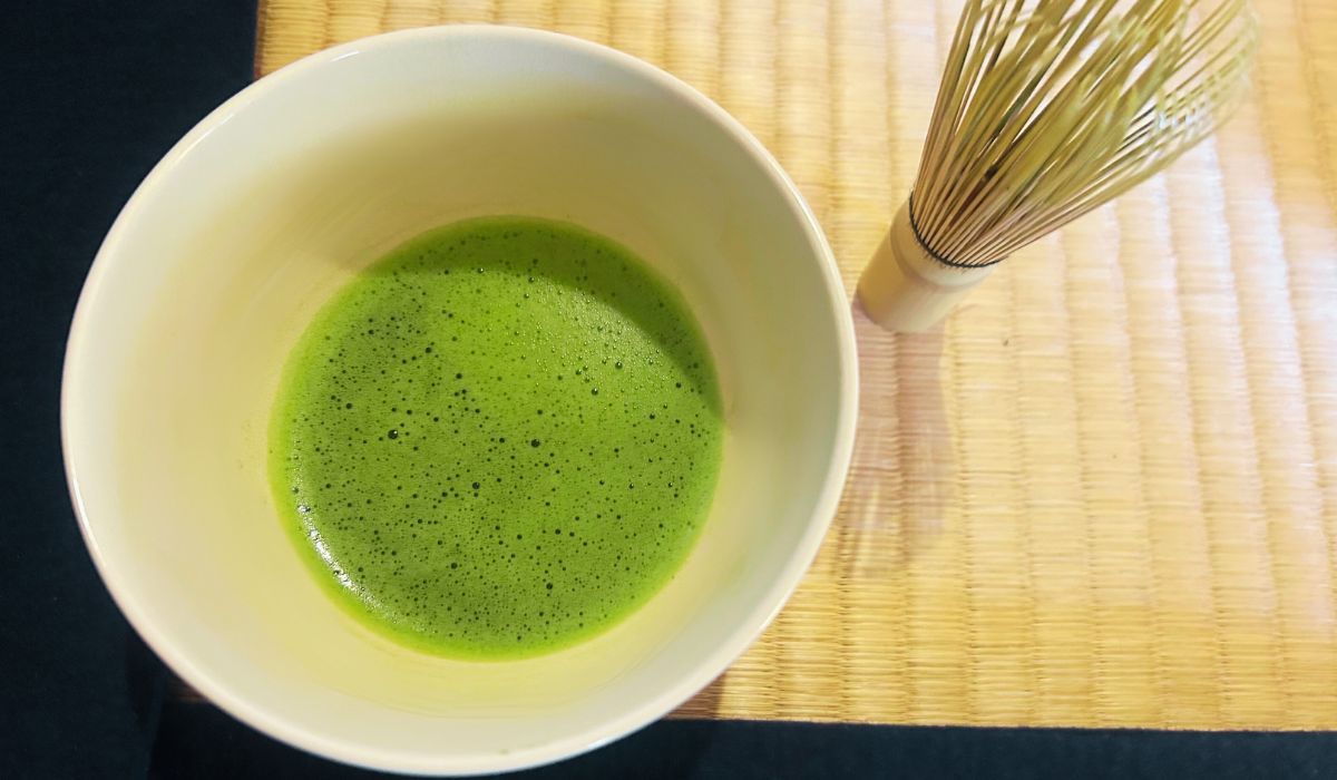 A bowl of matcha and a bamboo whisk on a traditional Japanese tatami floor