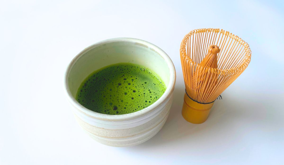 A bowl of matcha green tea with a bamboo whisk by its side