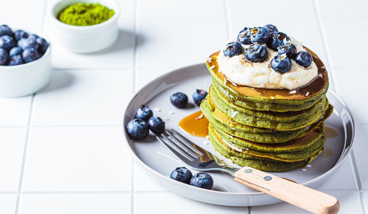 Stack of matcha pancakes with cream, blueberries, and maple syrup on top