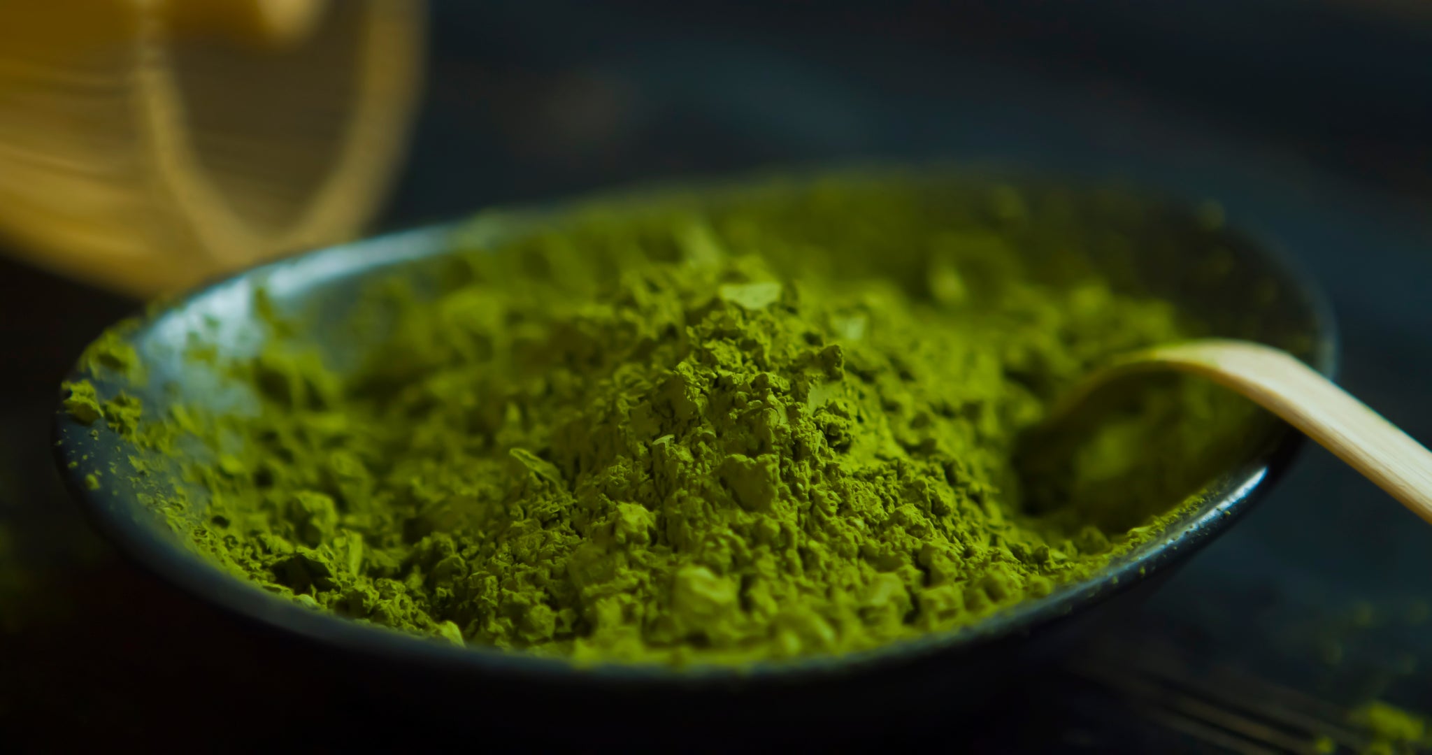 Vibrant green matcha green tea powder in a bowl with a bamboo matcha scoop