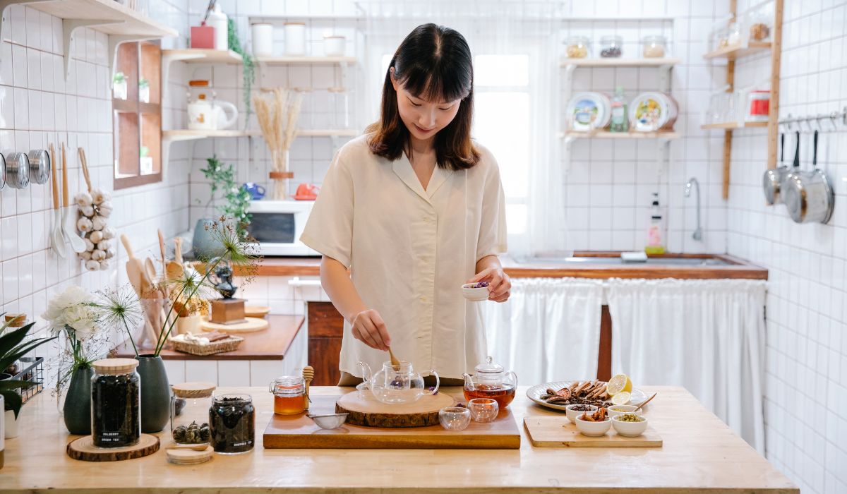 A woman brewing loose leaf green tea, including measuring the tea, heating the water, and steeping.