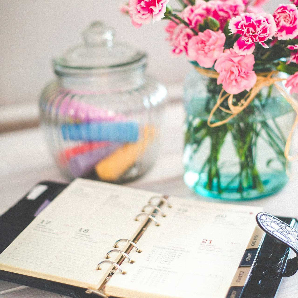 Date planner organizer with flowers and glass jar in background