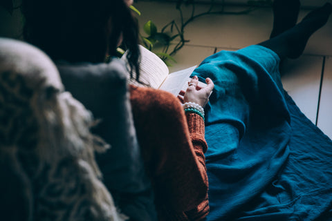 Girl sitting down with a blanket and reading a book