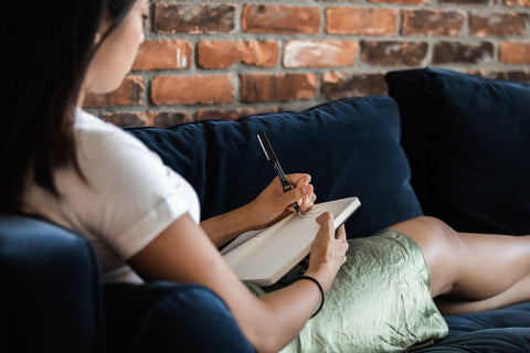 Girl lying on a sofa writing in a notebook