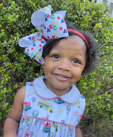 little girl wearing a Wee ones back to school hair bow with a red headband.