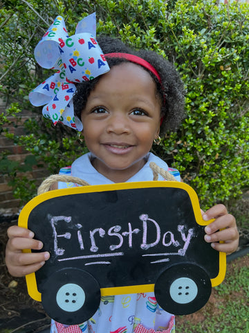 Little girl holding first day of school sign wearing a Wee Ones back-to-school hair bow.