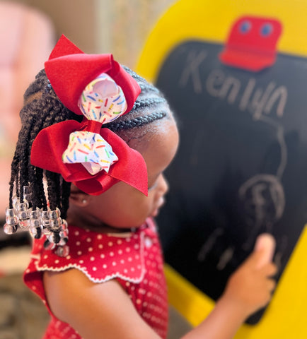 little girl playing school writing on a chalkboard wearing a big red and back to school hair bow from Wee Ones