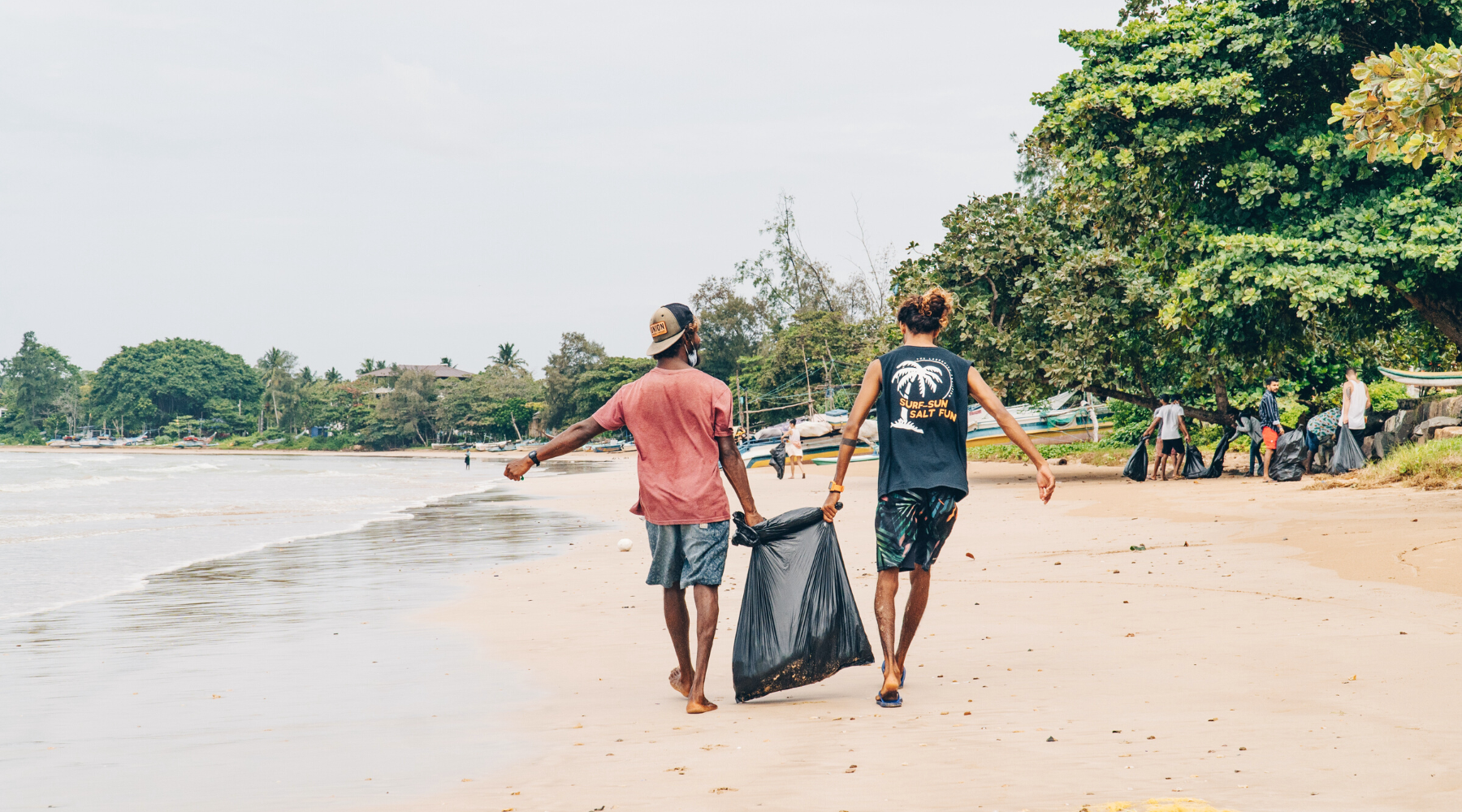 Two people carrying a black garbage bag on the beach 