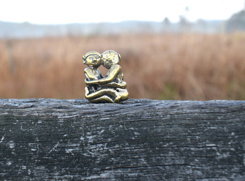 Small solid bronze ornament of lovers embracing each other resting on weathered timber