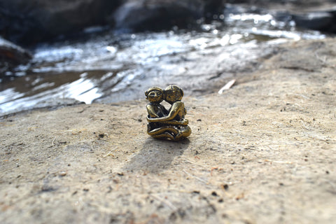 Small solid bronze ornament of lovers embracing each other resting on ground with creek in background