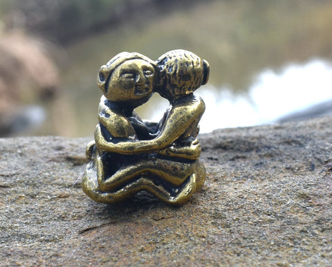 Small solid bronze ornament of lovers embracing each other resting on rock with water in background