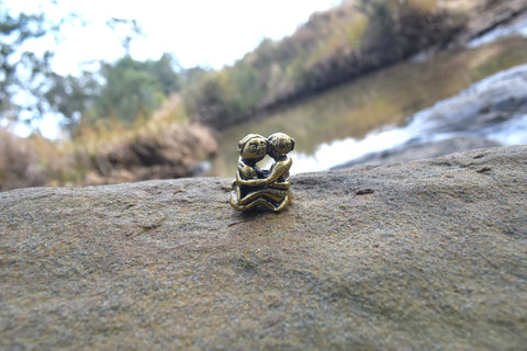 Small solid bronze ornament of lovers embracing each other resting on rock with creek in background