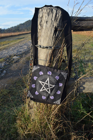 Black shoulder bag with white pentagram and pentacle of celtic knots surrounded by purple roses hanging on a weathered stump and chains