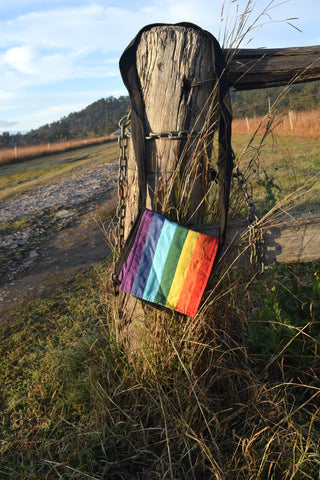 Shoulder bag with stips of purple, blue, green, yellow, orange and red fabric sewn together to make a rainbow LGBTQ tote hanging on a weathered stump with chains