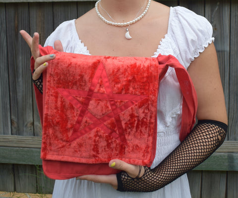 Person holding a red orange shoulder bag with a satin ribbon pentagram sewn on the front