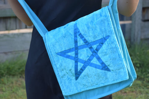 Person holding a sky blue shoulder bag with a satin ribbon pentagram sewn on the front