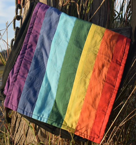 A rainbow shoulder bag with individually sewn colours hanging on a weathered post