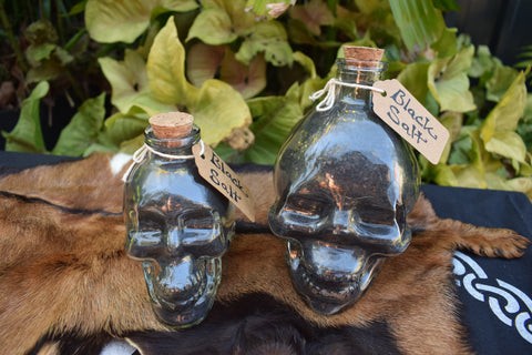 Two skull shaped glass jars filled with black salt rest on a brown goatskin.