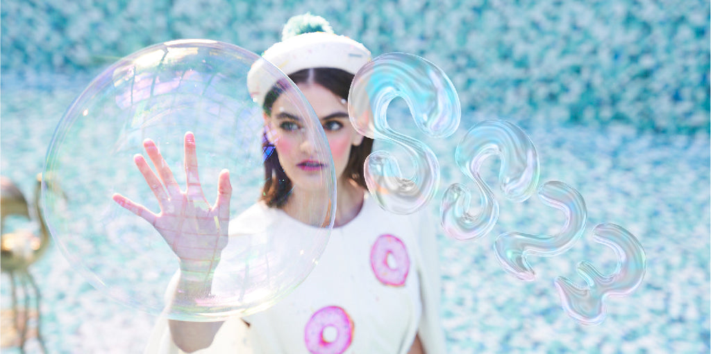 Editorial Image of a Girl Wearing a White Cape with Donuts and a Sprinkles-Pom Pom Beret from Underwater SS/23