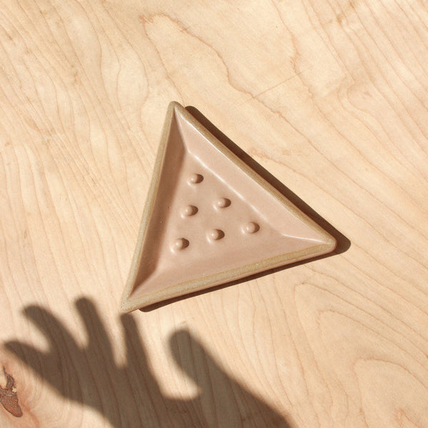 A ceramic triangular soap dish with a shadow hand against wood grain