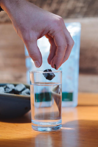 una mano soltando un cubo de espirulina congelada sobre un vaso con agua