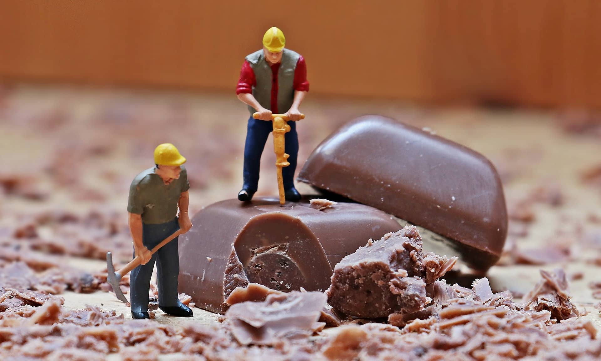 Miniaturfiguren arbeiten an zwei großen Stücken Schokolade