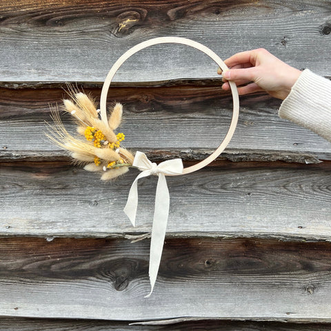 hand holding wooden wreath, adorned with yellow dried flowers