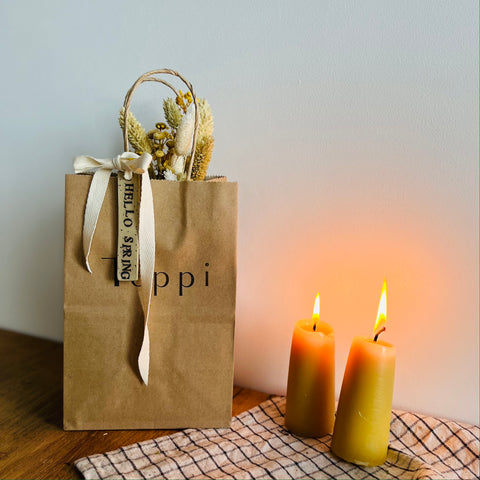 brown paper bag holding yellow bouquet, with a spring tag tied around the handles