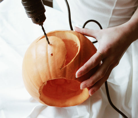 hand holding a drill to a carved pumpkin