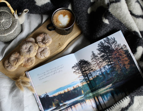 cosy flat lay of a book, teapot and tray of biscuits on a blanket