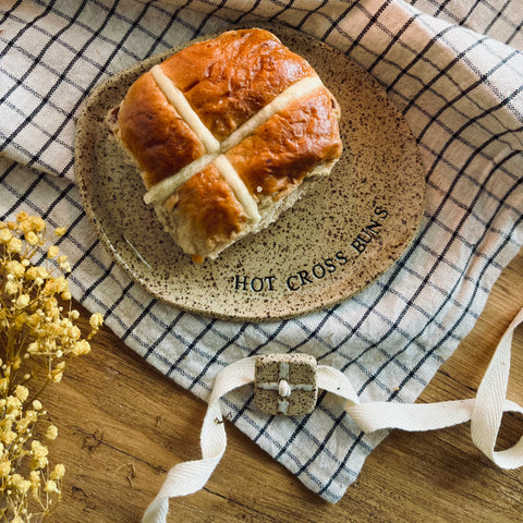 hot cross bun on a speckled ceramic plate with the words 'Hot Cross Buns' stamped into it