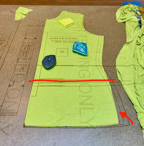 A flat lay of the tee shirt body front is shown on a cutting table, with the pattern projected onto it. An arrow indicates where the hipline has been blended from the base size to two sizes smaller at the full hip.
