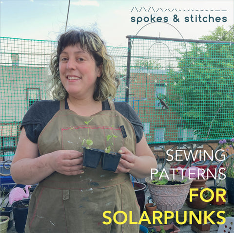 Sewing Patterns for Solarpunks. I'm standing on my porch wearing a Split Splat Apron and Arm Candy Tee, holding a seedling.