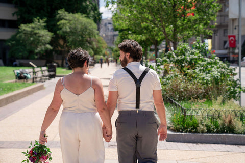 Two people in wedding attire are shown from the back, walking away from the camera.