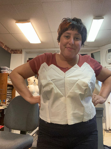 A person holds a muslin bodice against her own torso to check the fit of the drape.