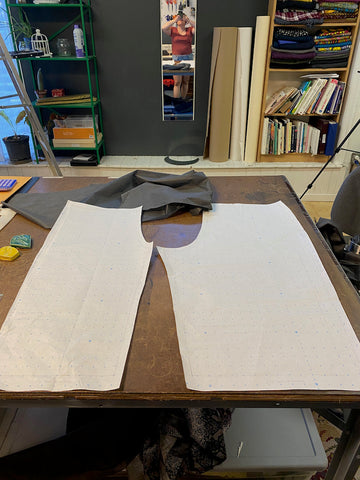 A paper pants pattern is laid out across a large cutting table. Ruby's reflection is visible in the mirror behind the table.