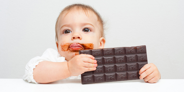 A cute baby joyfully holds a piece of chocolate, savoring the sweet treat with delight and innocence.