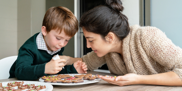 A woman and a boy enjoying cookies together at a table, savoring the sweet moments of togetherness.