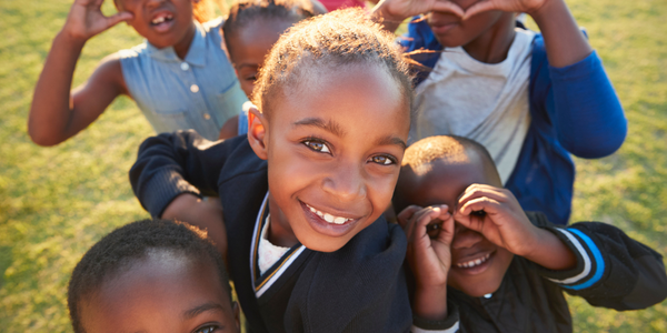 A group of children happily smiling and forming a heart shape with their hands.